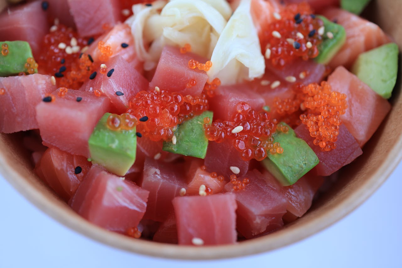 hero-img-02 Colorful poke bowl with tuna, avocado, red caviar, and sesame seeds in a wooden bowl.