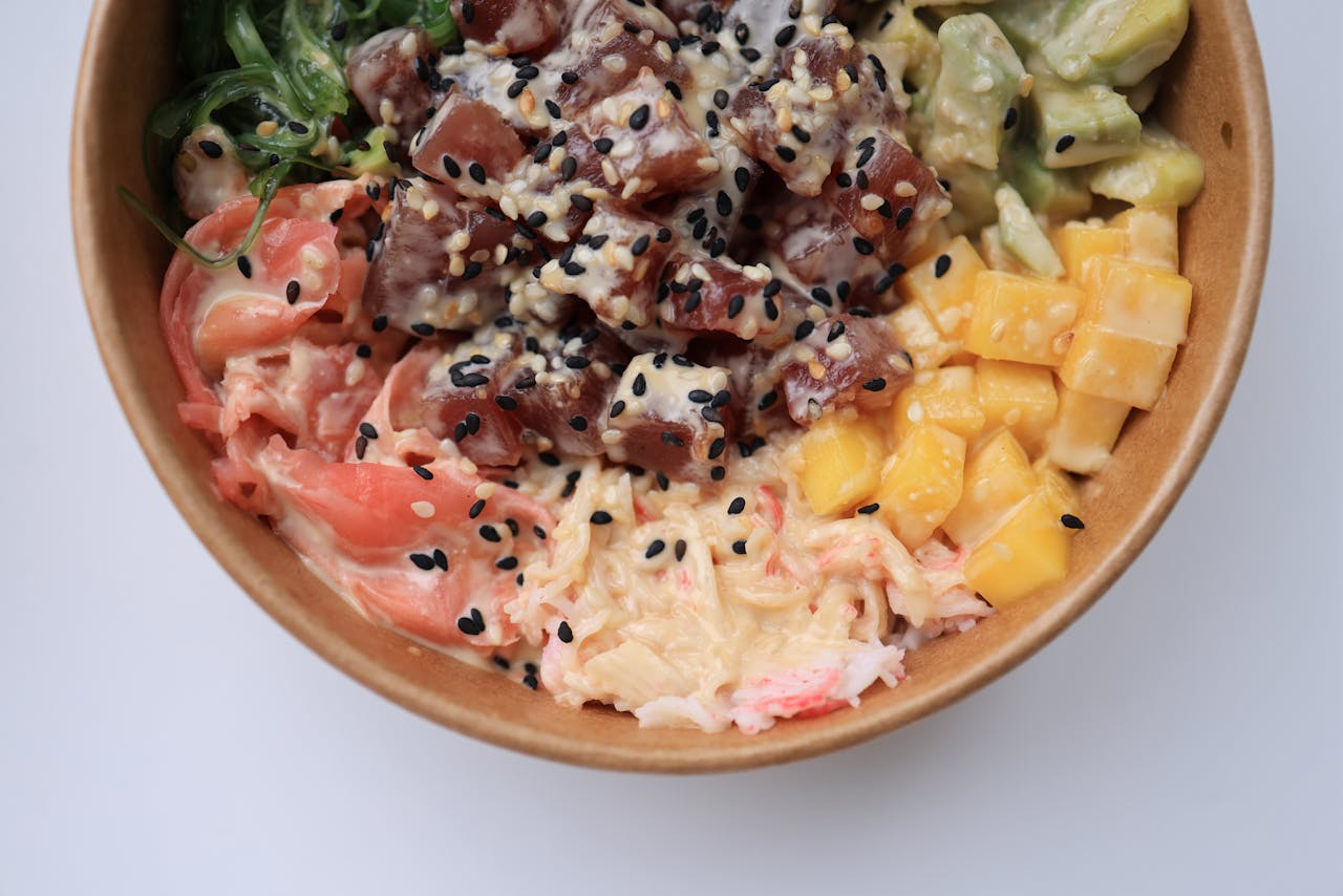 hero-img-01 Delicious poke bowl filled with fresh tuna, mango, avocado, and seaweed on a white background.
