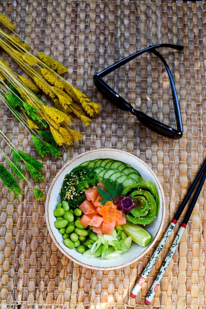 gallery-5 Colorful sushi bowl with fresh vegetables, chopsticks, and sunglasses on a woven mat. Perfect for healthy food concepts.